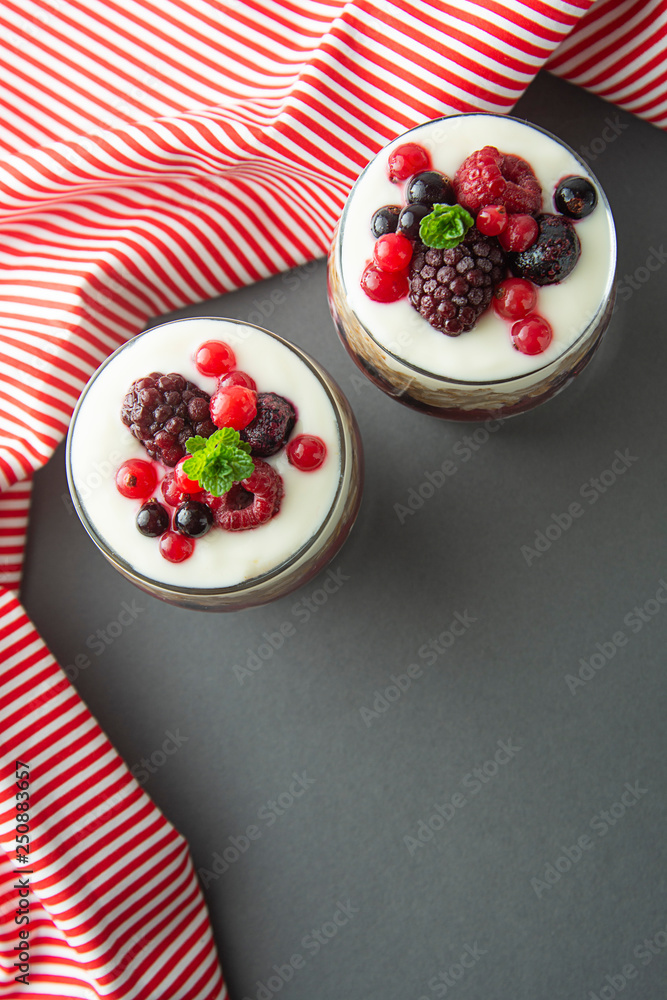 Two jars with oatmeals granola and berries and yogurt over gray background with copy space. Vertical image. Two jars with oatmeals granola and berries and yogurt over gray background with copy space. Vertical image.