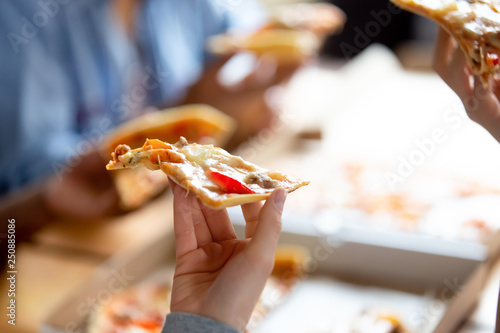 Close up female hand holding piece of pizza, friends together in cafe