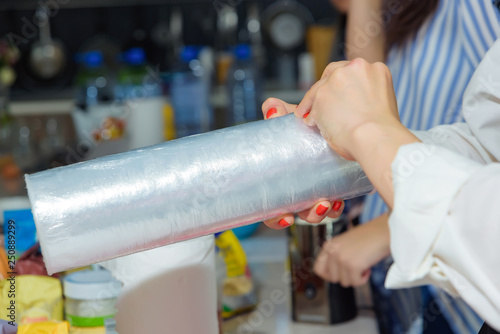 Woman holding a plastic wrap. Cooking in the kitchen. Transparent thin film for products. Red manicure girl.