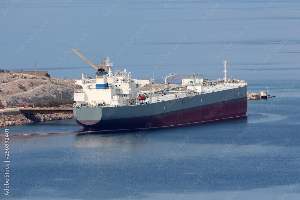 International oil tanker parked in local harbour waiting to be unloaded surrounded with calm dark blue sea and stone shore on warm sunny day International oil tanker parked in local harbour waiting to be unloaded surrounded with calm dark blue sea and stone shore on warm sunny day