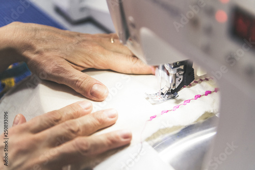 Close up view of hands of a lady working in her laboratory. Woman sews with sewing machine creates accessories repairs mend clothes embroider and packs trendy clothes. Works at home. Leisure time