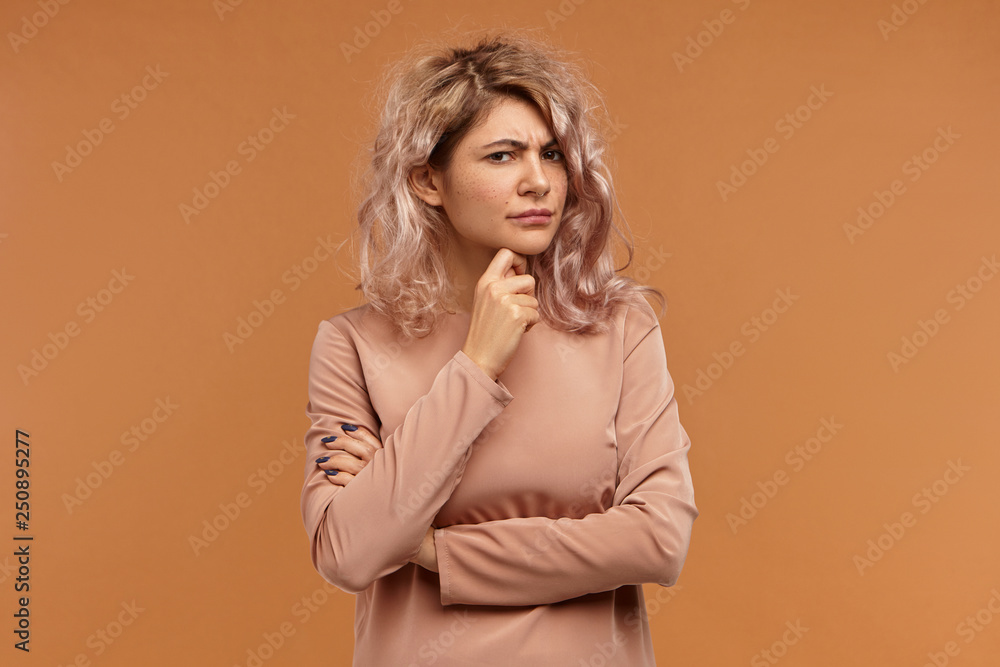 Let me think. Picture of frowning serious young woman with pinkish hair holding hand on her chin, having concentrated pensive facial expression, trying to remember something that she forgot Let me think. Picture of frowning serious young woman with pinkish hair holding hand on her chin, having concentrated pensive facial expression, trying to remember something that she forgot