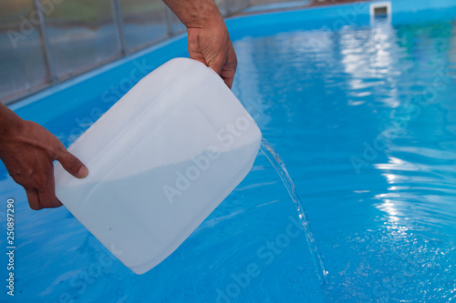 Φωτογραφία men's hands pour light liquid from a plastic tank into a pool, into water
