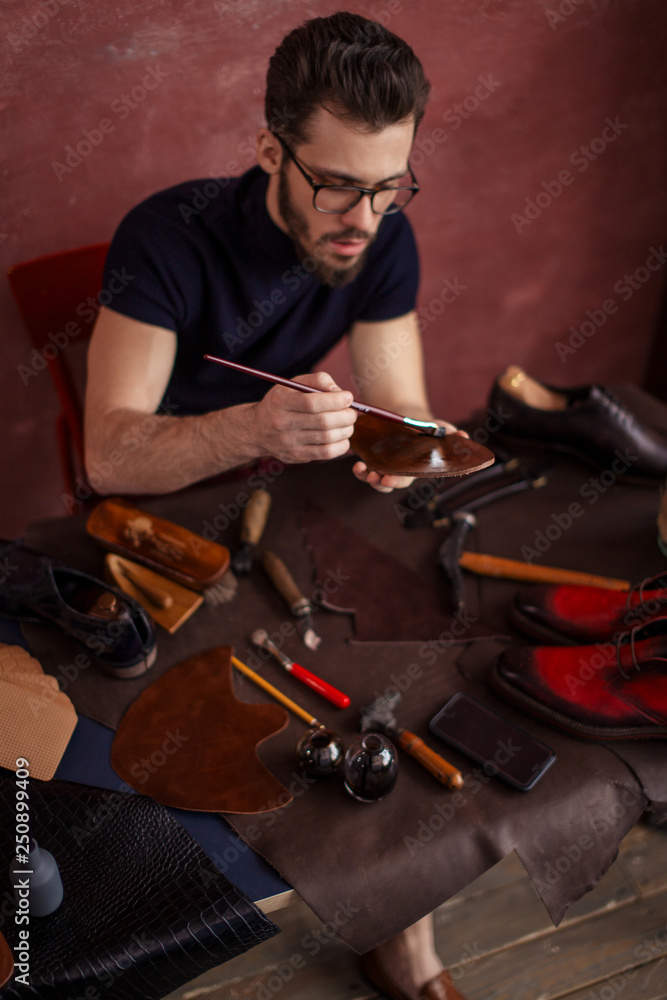 young designer using a brush while working in the shoe shop with moderrn interior. close up photo young designer using a brush while working in the shoe shop with moderrn interior. close up photo