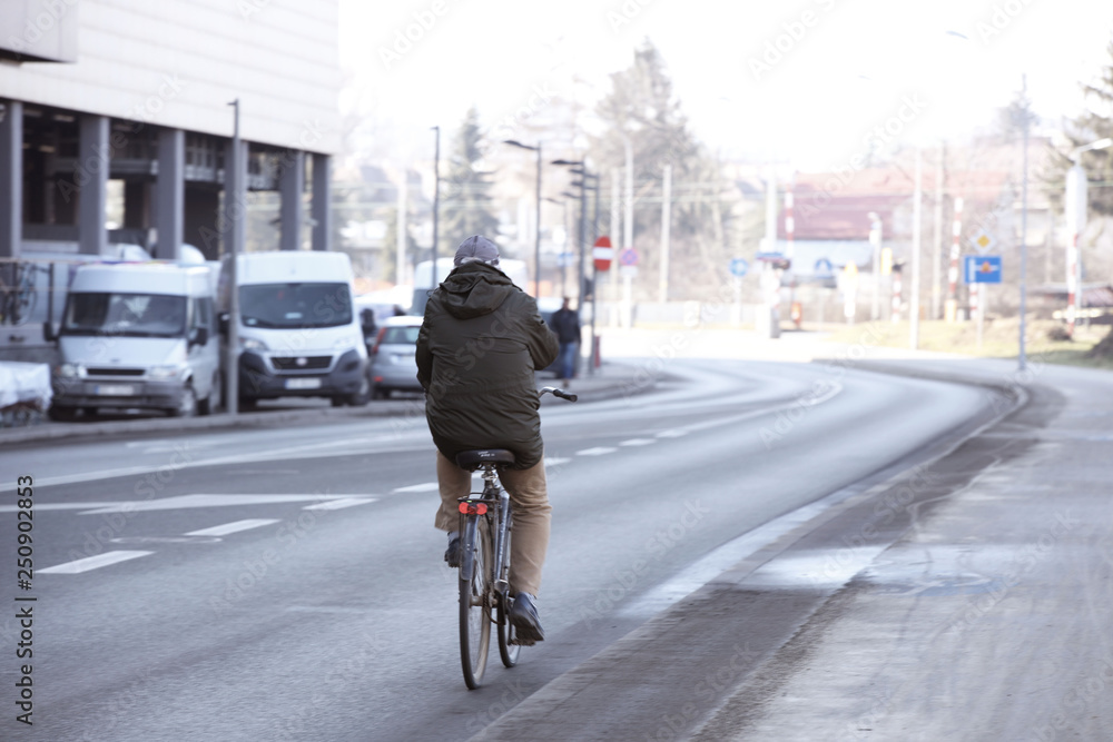 A man rides a bicycle along an asphalt city road near a shopping center with a truck parking. The worker gets to work in the morning at rush hour on environmental transport. Healthy lifestyle A man rides a bicycle along an asphalt city road near a shopping center with a truck parking. The worker gets to work in the morning at rush hour on environmental transport. Healthy lifestyle