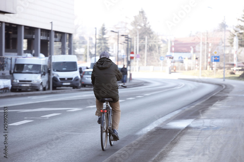 A man rides a bicycle along an asphalt city road near a shopping center with a truck parking. The worker gets to work in the morning at rush hour on environmental transport. Healthy lifestyle
