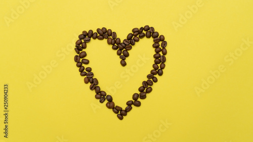 Heart made of coffee beans in the center of yellow background