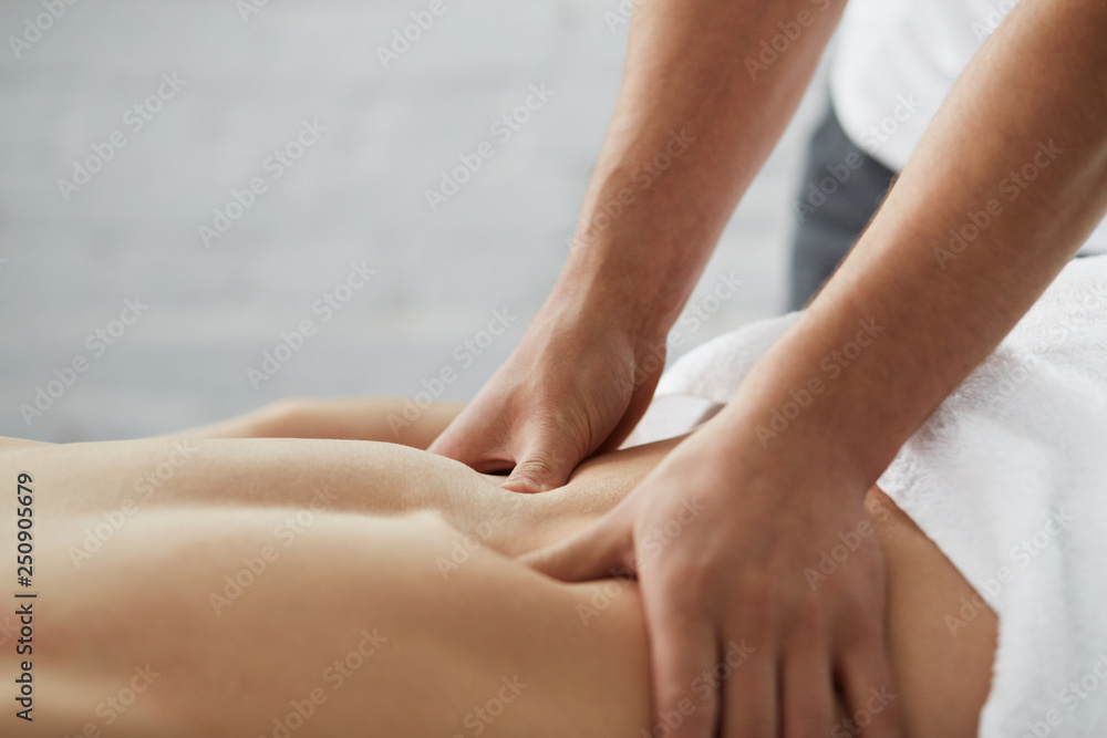 Young handsome man enjoying a back massage. Professional massage therapist is treating a male patient in apartment. Relaxation, beauty, body and face treatment concept. Home massage. - obrazy, fototapety, plakaty 