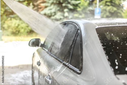 Side window of car washed in self serve carwash, high pressure jet water spraying on glass.