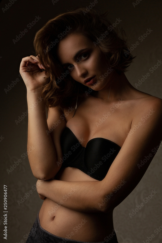 Dramatic portrait of awesome brunette model with wavy hair wears bra, posing in the shadows Dramatic portrait of awesome brunette model with wavy hair wears bra, posing in the shadows
