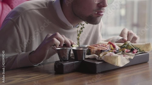 Handsome man in glasses eating his food without using cutlery close up. The client eating grilled fish served in cafe. Confident man rests in modern restaurant