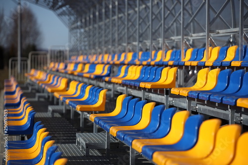 New stands on the football field of metal light construction with plastic seats in blue and yellow. Places for fans in the stadium. Going to the audience for sports competitions. Shelter from the run