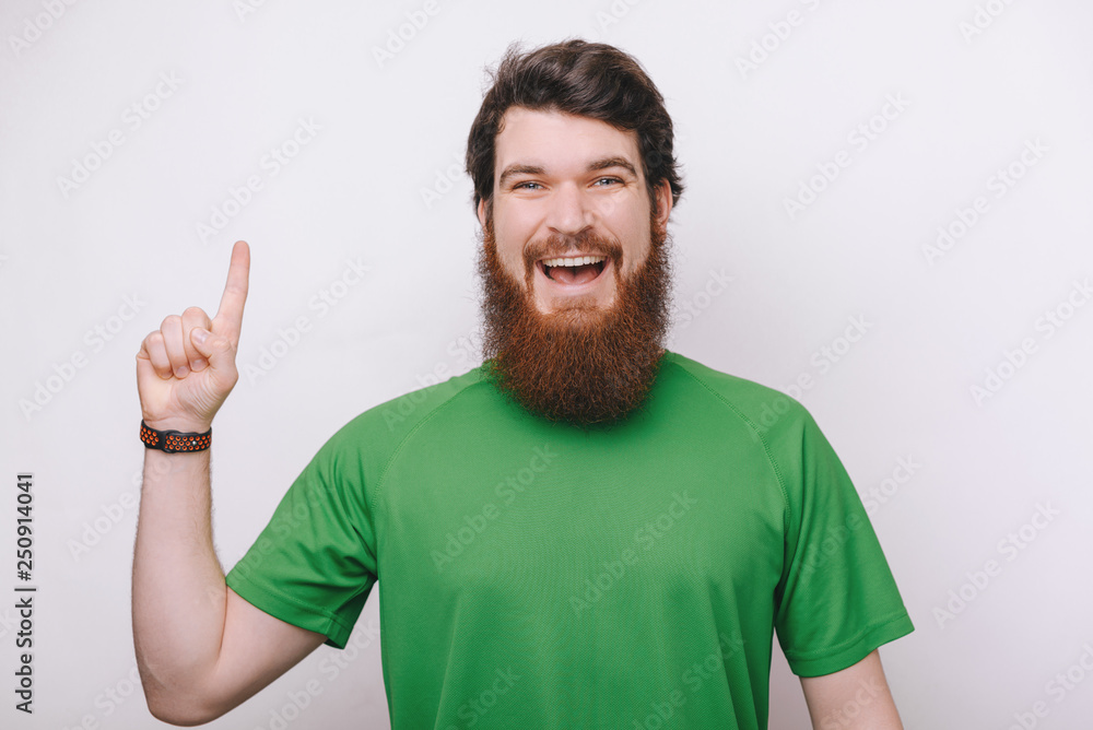 Portrait of an excited bearded man pointing finger up at copyspace isolated over gray background Portrait of an excited bearded man pointing finger up at copyspace isolated over gray background