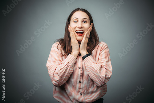 Surprised cute businesswoman touhing her face an looking at camera on gray background photo