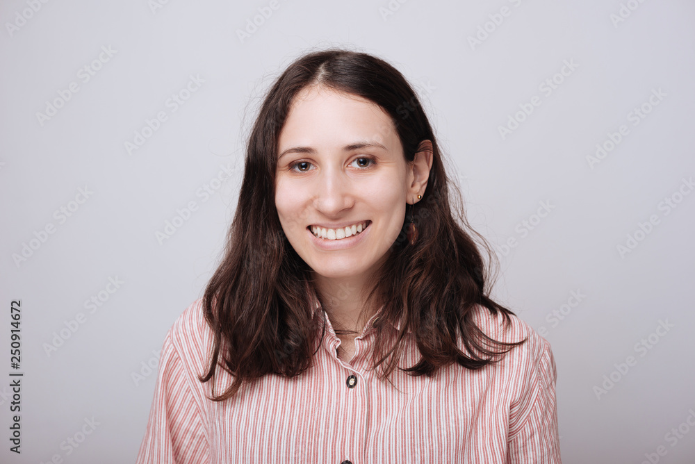 Beautiful smiling woman with clean skin, natural make-up, and white teeth on grey background Beautiful smiling woman with clean skin, natural make-up, and white teeth on grey background