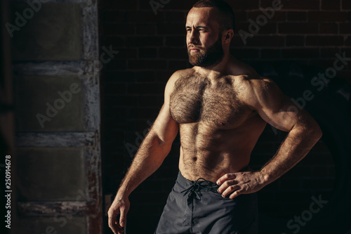Portrait of shirtless athletic bare chested male showing biceps and posing in a fitness studio on dark background