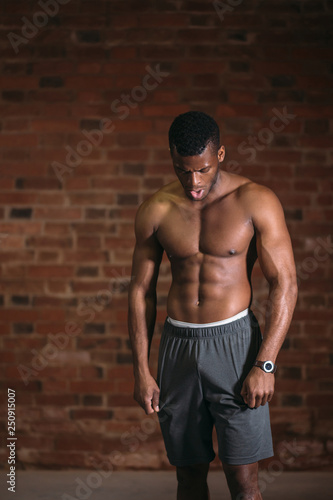 Strong afroamerican athletic man with naked perfect shape musculs standing isolated over brick background.