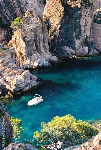 White motor boat sailing between rocks on the sunset in Spain