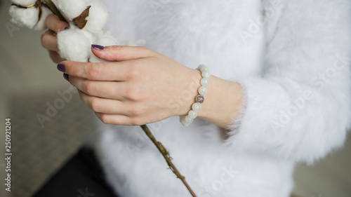 bracelet on hand, bracelet from pearls on hand, girl touches bracelet on hand, bracelet from white beads, girl holding a branch of cotton (horizontally, close up).