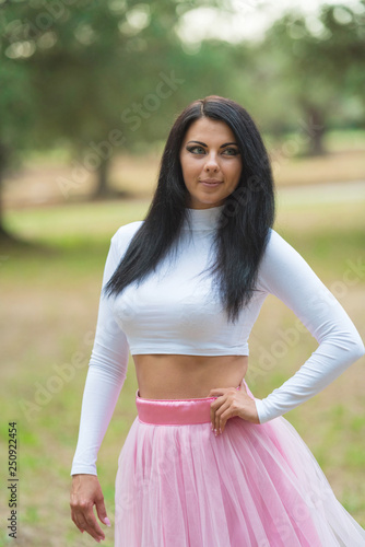Beautiful young woman in pink dress posing among olive trees in garden