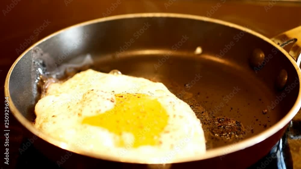 Fresh egg with ground pepper is frying in a hot fry pan as steam rises. Close up with zoom out and selective focus. Fresh egg with ground pepper is frying in a hot fry pan as steam rises. Close up with zoom out and selective focus.