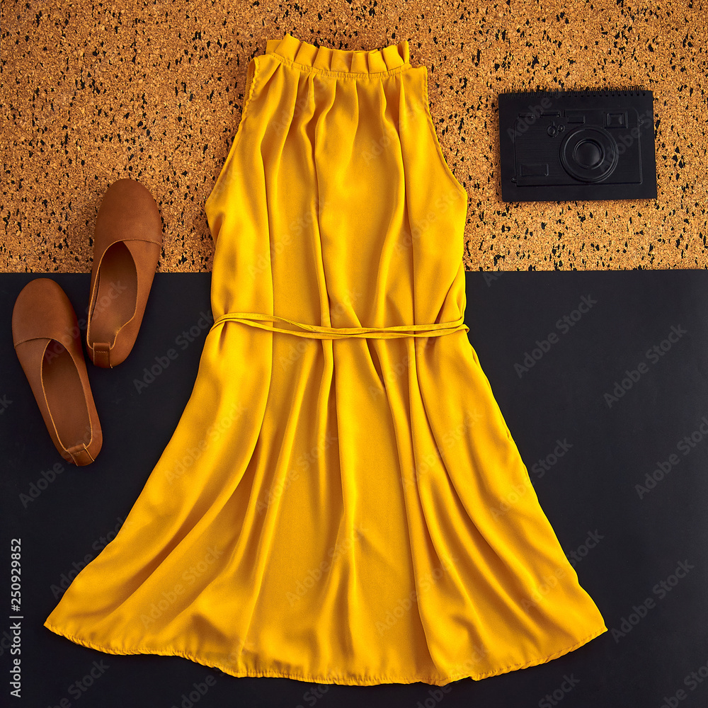 Layout with clothes in brown orange yellow warm tones. Feminine beautiful stylish mustard dress with open shoulders. Simple brown shoes without heel and unusual black notebook in form of camera. Photo...
