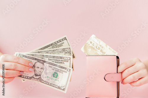 Dollars and pink wallet with credit card in woman's hands on pink background