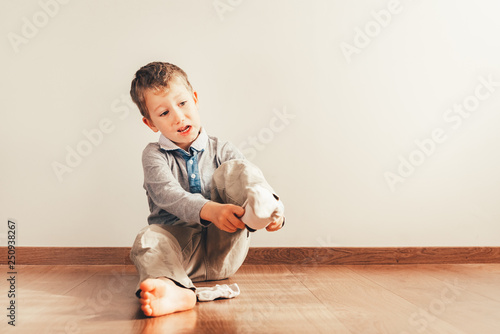 Child with lots of independence sitting on the floor putting on his socks with an expression of effort