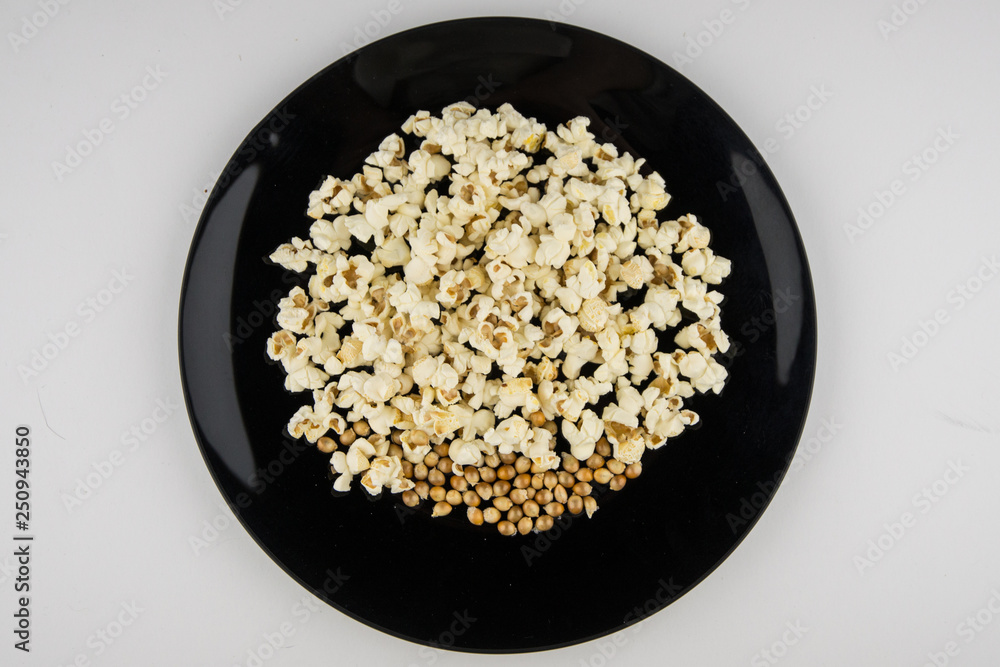Cooked in the microwave popcorn in a black bowl on a white. unprepared grains remained lying down Cooked in the microwave popcorn in a black bowl on a white. unprepared grains remained lying down