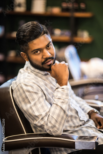 Handsome bearded indian man with new haircut sitting in chair at the barbershop