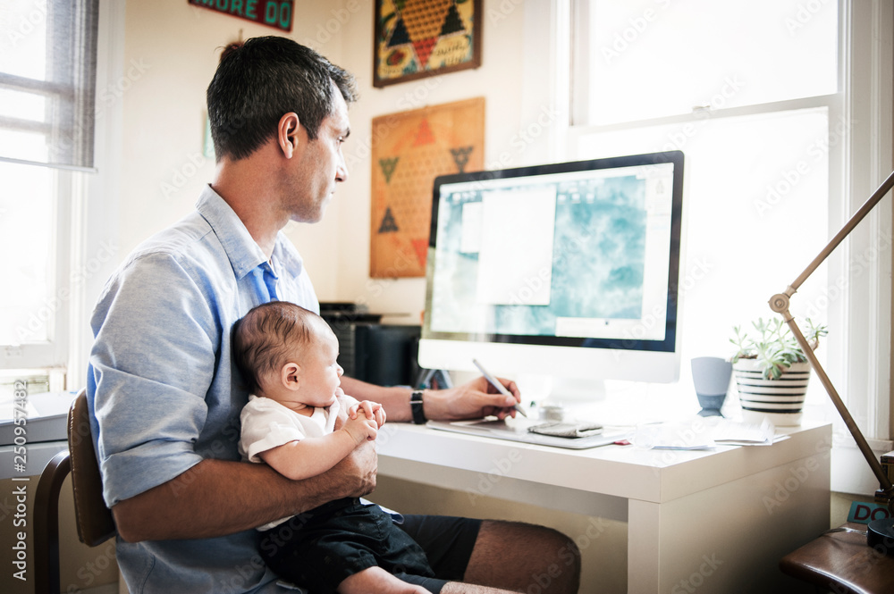 Father sitting with his baby son (2-5 months) at desk Father sitting with his baby son (2-5 months) at desk