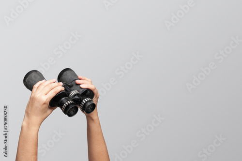 Hands holding binoculars on gray background