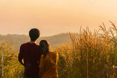 Asian woman and man standing together in meadow and looking far away at sunrise time, Selective focus, Copy space.