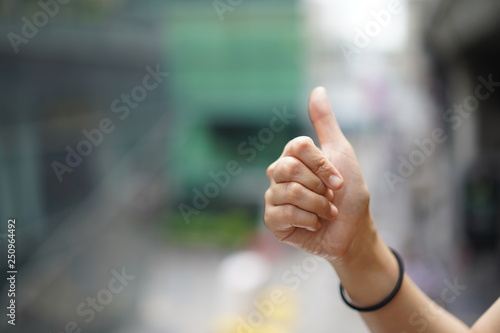 Women raise up the thumb with blur green background near sky train, Bangkok, Thailand.