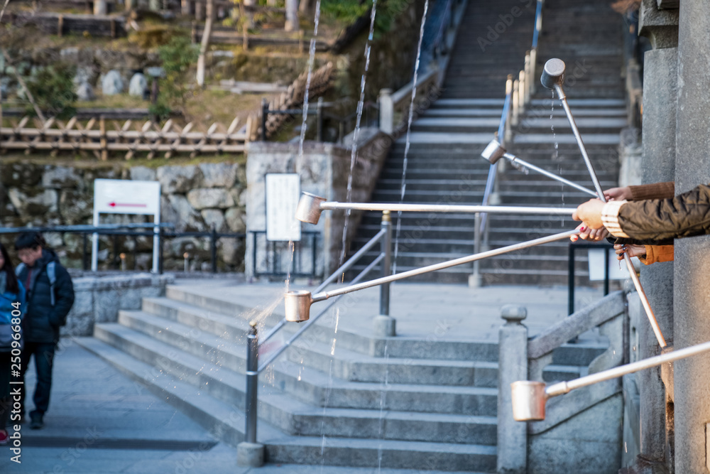 Close up people hand try to scooping water from 3 holy water line with long handle cup in Kiyomizu-dera temple, Japan Close up people hand try to scooping water from 3 holy water line with long handle cup in Kiyomizu-dera temple, Japan