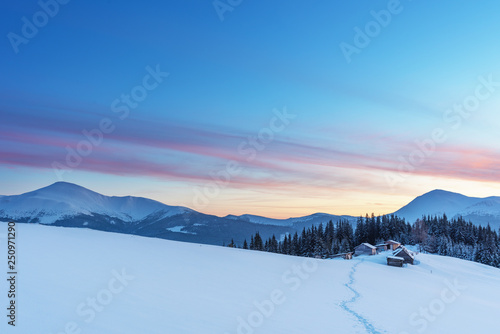 A colorful evening with a beautiful sunset and dusk in the snow-covered mountains of the mountains with mountain houses in the Ukrainian Carpathians overlooking Hoverla and Petros.