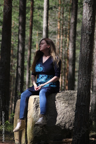 A woman sitting on a big stone in a forest enjoying the sun