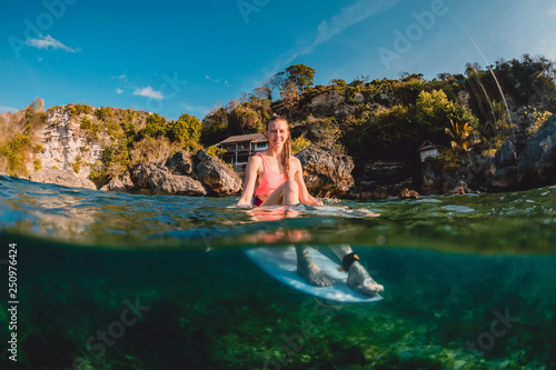 Attractive surfer girl with surfboard. Surfer sit at board in ocean.