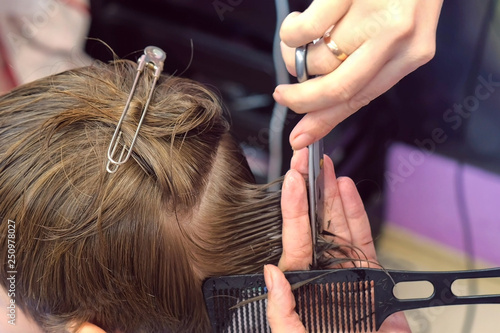 Hairdresser cutting hairs with scissors on boy's head. Top view, stylist's hands close-up.