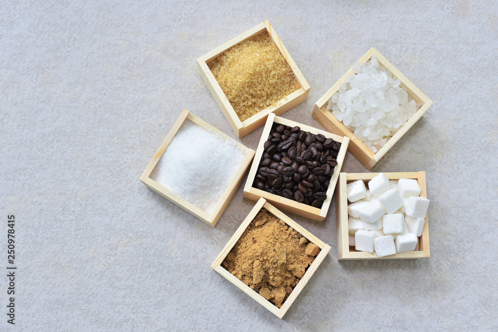 Roasted coffee beans and wooden box of brown sugar, raw sugar, cube sugar, rock sugar and white granulation sugar arround . sucrose or table sugar are the nutritive sweeteners.