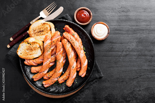 Grilled sausages and different sauce on a dark wooden background.