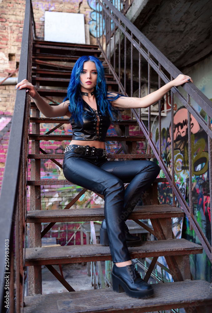 Foto Stock Beautiful rock girl with blue hair (informal model), dressed in  black leather pants and topic, sits on staircase | Adobe Stock