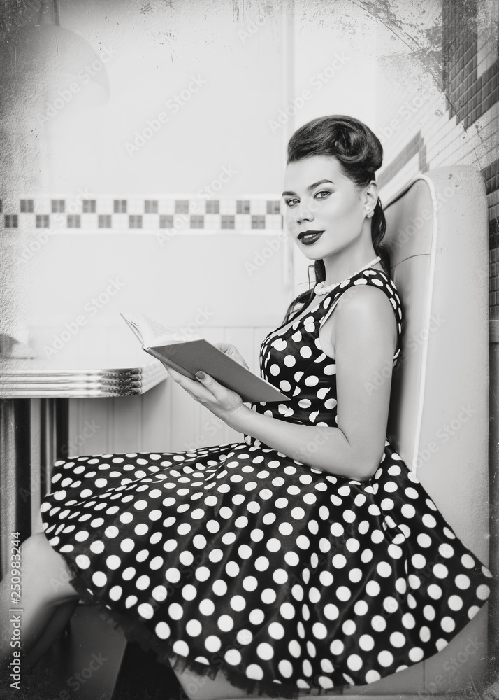 Retro (vintage) portrait of cute young woman sitting in cafe with book. Pin  up style portrait of young woman in dress, black and white, texture effect  Stock Photo