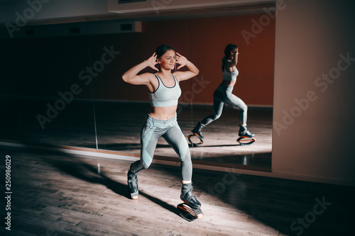 Smiling young sporty Caucasian brunette doing exercises with kangoo jumps footwear.