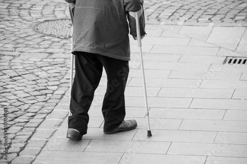 closeup of aged man walking with sticks in the street on cobblestone on back view
