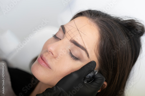 Beautician in the saloon doing the perfect architecture of eyebrows.