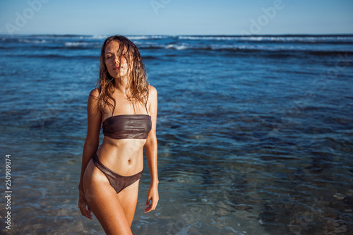 girl with wet hair in a swimsuit is standing in the water on the beach