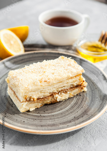 Slice of classical dessert napoleon cake on a gray plate with a cup of tea