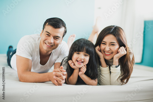 Young mother father or parent and daughter enjoying with lie on the stomach in the white bed at home, happy family smiling, blue background