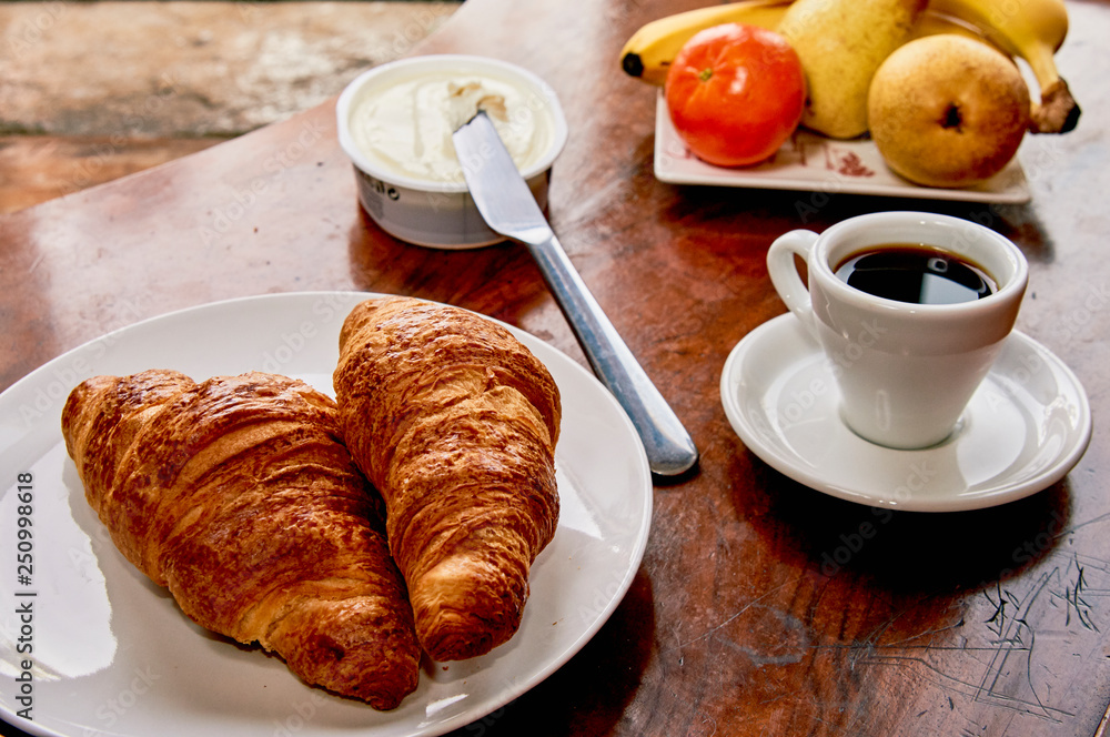 Coffee and croissant breakfast on a vintage wooden table. Espresso, croissants, cream cheese and fruits. 
